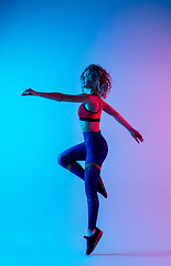Image showing Young sportive woman training isolated on gradient pink-blue studio background in neon light.