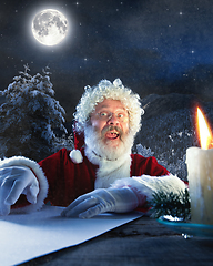 Image showing Emotional Santa Claus congratulating with New Year and Christmas, writing a letter, wish list in midnight with candle