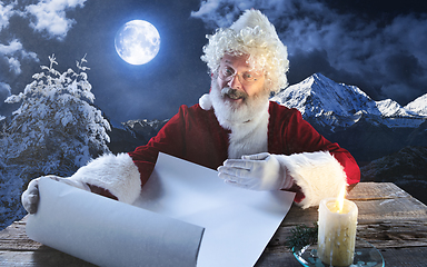 Image showing Emotional Santa Claus congratulating with New Year and Christmas, writing a letter, wish list in midnight with candle