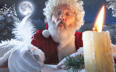 Image showing Emotional Santa Claus congratulating with New Year and Christmas, writing a letter, wish list in midnight with candle