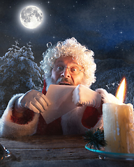 Image showing Emotional Santa Claus congratulating with New Year and Christmas, sending a letter, wish list in midnight with candle