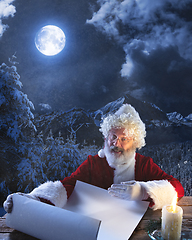 Image showing Emotional Santa Claus congratulating with New Year and Christmas, writing a letter, wish list in midnight with candle