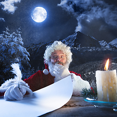 Image showing Emotional Santa Claus congratulating with New Year and Christmas, writing a letter, wish list in midnight with candle