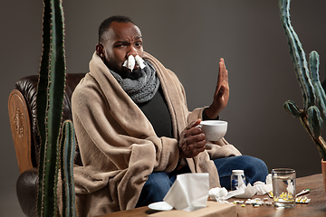 Image showing Young African-American man wrapped in a plaid sitting at home trying to protect from somebody\'s sick