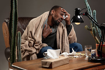 Image showing Young African-american man wrapped in a plaid looks sick, ill, has terrible headache sitting at home indoors.