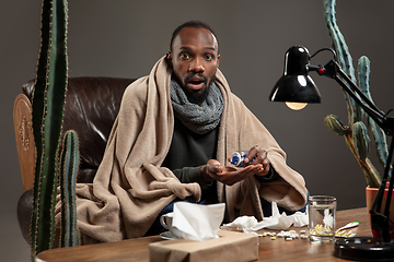 Image showing Young African-american man wrapped in a plaid looks sick, ill sitting at home indoors.