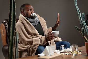 Image showing Young African-American man wrapped in a plaid sitting at home trying to protect from somebody\'s sick