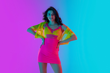 Image showing Portrait of beautiful seductive girl in fashionable bright outfit on colour gradient pink-blue background in neon light.