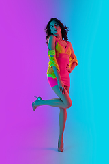 Image showing Beautiful seductive girl in fashionable crimson and yellow outfit on bright gradient pink-blue background in neon light