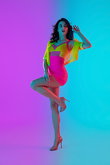 Image showing Beautiful seductive girl in fashionable crimson and yellow outfit on bright gradient pink-blue background in neon light