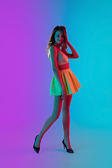 Image showing Beautiful seductive girl in fashionable bright summer outfit posing on colour gradient pink-blue background in neon light.