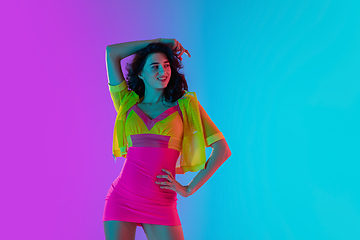 Image showing Portrait of beautiful seductive girl in fashionable bright outfit on colour gradient pink-blue background in neon light.