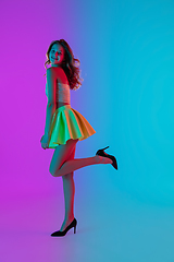 Image showing Beautiful seductive girl in fashionable bright summer outfit posing on colour gradient pink-blue background in neon light.