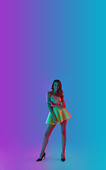 Image showing Beautiful seductive girl in fashionable bright outfit posing on colour gradient pink-blue background in neon light.