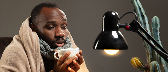 Image showing Man wrapped in a plaid looks sick, ill, sneezing and coughing sitting at home indoors