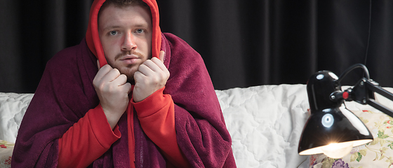 Image showing Man wrapped in a plaid looks sick, ill, sneezing and coughing sitting at home indoors