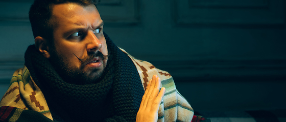 Image showing Man wrapped in a plaid looks sick, ill, sneezing and coughing sitting at home indoors
