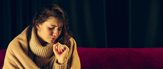 Image showing Woman wrapped in a plaid looks sick, ill, sneezing and coughing sitting at home indoors