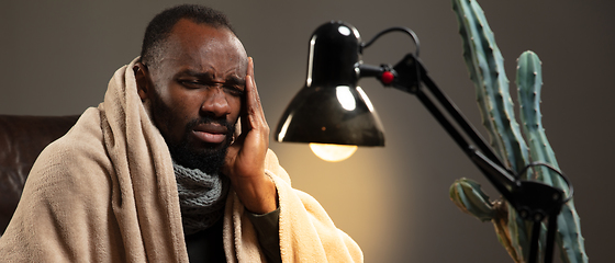 Image showing Man wrapped in a plaid looks sick, ill, sneezing and coughing sitting at home indoors