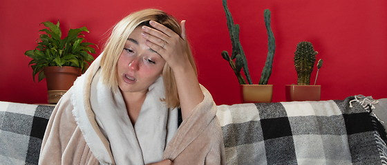 Image showing Woman wrapped in a plaid looks sick, ill, sneezing and coughing sitting at home indoors