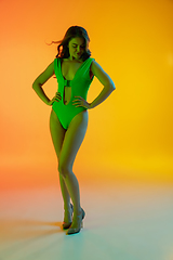 Image showing Beautiful seductive girl in fashionable green swimsuit on bright gradient yellow-orange background in neon light