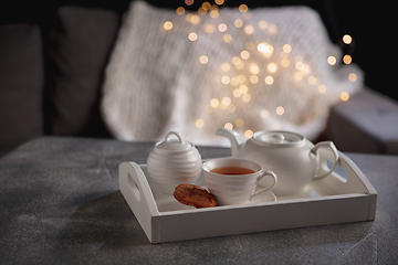 Image showing Cozy winter. White wooden tray with tea set on grey table with led garland lights. The concept of home atmosphere and comfort.