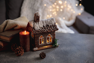 Image showing Winter house miniature illuminated and books on grey and white background. The concept of home atmosphere and comfort.