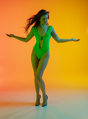 Image showing Full-length portrait of beautiful seductive girl in fashionable green swimsuit on bright gradient background in neon light