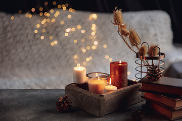 Image showing Burning candles in the wooden box isolated on grey and white background with garland lights. Greeting card design.