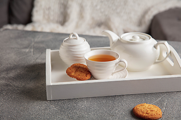 Image showing White wooden tray with tea set on grey table. The concept of home atmosphere and comfort.