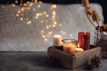 Image showing Burning candles in the wooden box isolated on grey and white background with garland lights. Greeting card design.