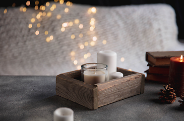 Image showing Burning candles in the wooden box isolated on grey and white background with garland lights. Greeting card design.