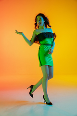 Image showing Beautiful seductive girl in fashionable, modern outfit on bright gradient yellow-orange background in neon light