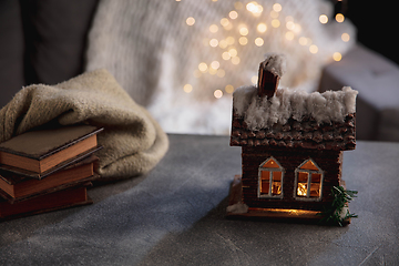 Image showing Winter house miniature illuminated and books on grey and white background. The concept of home atmosphere and comfort.