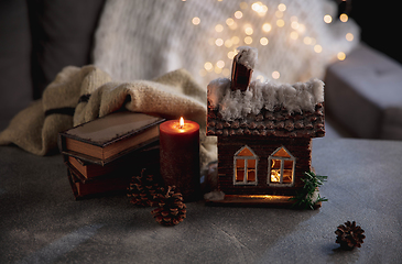 Image showing Winter house miniature illuminated and books on grey and white background. The concept of home atmosphere and comfort.