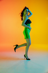 Image showing Beautiful seductive girl in fashionable, modern outfit on bright gradient yellow-orange background in neon light