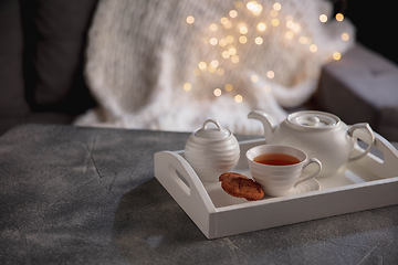 Image showing Cozy winter. White wooden tray with tea set on grey table with led garland lights. The concept of home atmosphere and comfort.