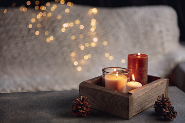 Image showing Burning candles in the wooden box isolated on grey and white background with garland lights. Greeting card design.