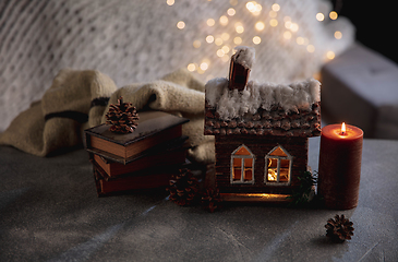 Image showing Winter house miniature illuminated and books on grey and white background. The concept of home atmosphere and comfort.