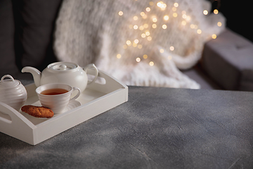 Image showing Cozy winter. White wooden tray with tea set on grey table with led garland lights. The concept of home atmosphere and comfort.