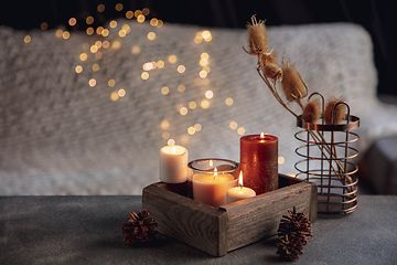 Image showing Burning candles in the wooden box isolated on grey and white background with garland lights. Greeting card design.