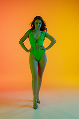 Image showing Beautiful seductive girl in fashionable green swimsuit on bright gradient yellow-orange background in neon light