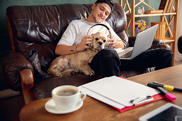 Image showing Young man playing with his dog pet and listening to music during Coronavirus or Covid-19 quarantine. Lifestyle concept.