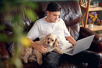 Image showing Young man working on laptop computer sitting at home with a dog pet and leaning during Coronavirus or Covid-19 quarantine