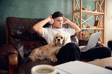 Image showing Young man playing with his dog pet and listening to music during Coronavirus or Covid-19 quarantine. Lifestyle concept.