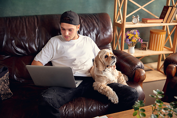 Image showing Young man working on laptop computer sitting at home with a dog pet and leaning during Coronavirus or Covid-19 quarantine