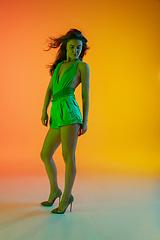 Image showing Beautiful seductive girl in fashionable, summer outfit, green jumpsuit on bright gradient yellow-orange background in neon light