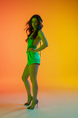 Image showing Beautiful seductive girl in fashionable, summer outfit, green jumpsuit on bright gradient yellow-orange background in neon light