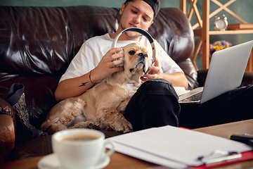 Image showing Young man sitting at home with his dog pet and listening to music during Coronavirus or Covid-19 quarantine. Lifestyle concept.