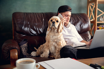 Image showing Young man working on laptop computer sitting at home with a dog pet and leaning during Coronavirus or Covid-19 quarantine